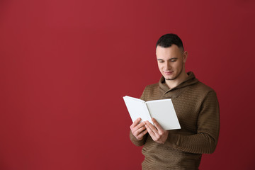 Handsome young man with book on color background