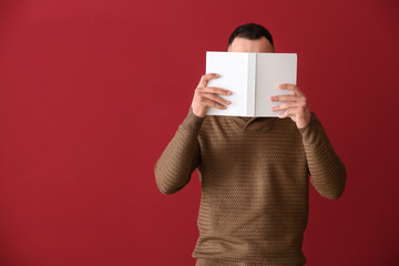 Handsome young man with book on color background