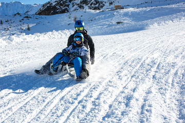Happy people, children and adults, sliding on a sunny day in Tyrol mountains