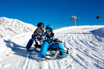 Happy people, children and adults, sliding on a sunny day in Tyrol mountains