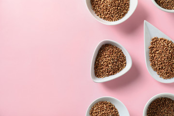 Bowls and plate with raw buckwheat on color background