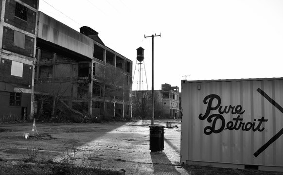 City Of Detroit With Dumpster With Abandoned Buildings Withe A Water Tower And Power Lines In Monchrome During The Day Outdoors.