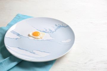 Plate with fried quail egg on white wooden table