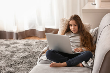 Cute little girl with laptop watching cartoons at home