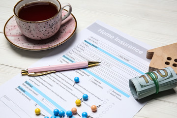 Home insurance form with dollar banknotes and cup of tea on white table