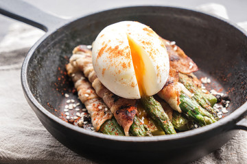 Frying pan with tasty bacon wrapped asparagus and egg on table, closeup