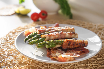 Plate with tasty bacon wrapped asparagus on table