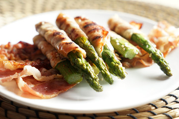 Plate with tasty bacon wrapped asparagus on table, closeup