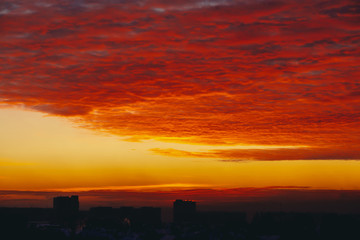 Cityscape with fiery blood vampire dawn. Amazing warm dramatic cloudy sky above dark silhouettes of city buildings. Orange sunlight. Atmospheric background of sunrise in overcast weather. Copy space.