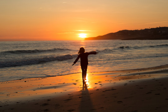 Happy child running on the beach during sunset, Praia da Luz, Algarve, Portugal