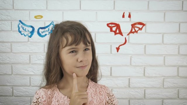 Angel or demon. A little girl is faced with the choice of angel wings or devil horns. Good and evil concept.