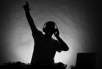 Silhouette of male DJ playing music on grey background