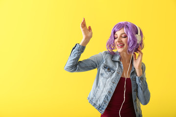 Beautiful young woman with headphones dancing against color background