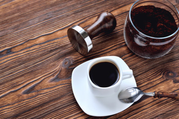 A cup of coffee on a saucer, a coffee spoon with a wooden handle, a tin can with ground coffee, a...