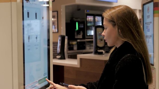 Woman customer store place orders and pay by contactless credit card mobile phone through self pay floor fast food, payment terminal touchscreen big cafe. Paypass.