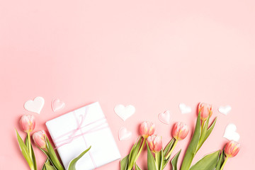 Romantic floral background with tulips flowers, gift and hearts on pink pastel background.