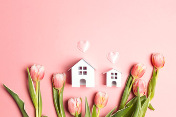 Two miniature white toy houses with tulip flowers on pink  background.