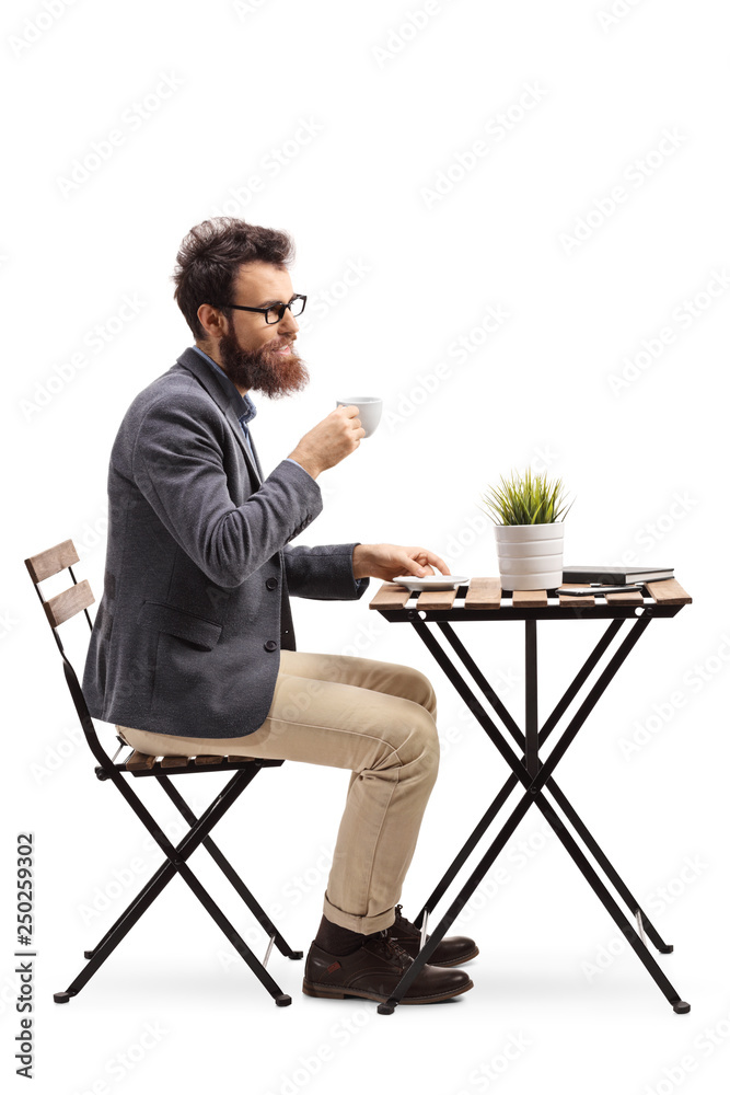 Wall mural young bearded man holding coffee cup and sitting at a table