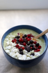 Fruit and vegetable smoothie (spinach, apple, banana, orange) with wild berries, chia seeds and coconut flake topping. Selective focus.