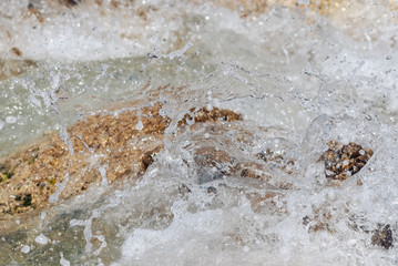 white splashes of sea water break on a brown block of stones. Selective focus macro shot with shallow DOF. Ocean, sea vacation background