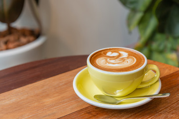 Hot cappuccino coffee in a yellow cup with latte art on the wooden table in the coffee shop.