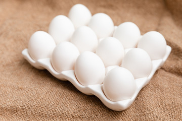 White Chicken Eggs In Ceramic Carton Holder On Burlap Background