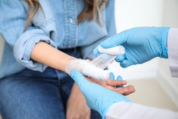 Doctor applying bandage onto finger of young woman, closeup