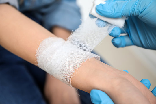 Doctor applying bandage onto wrist of young woman, closeup