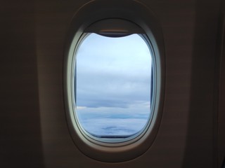 Airplane window with sky clouds view.