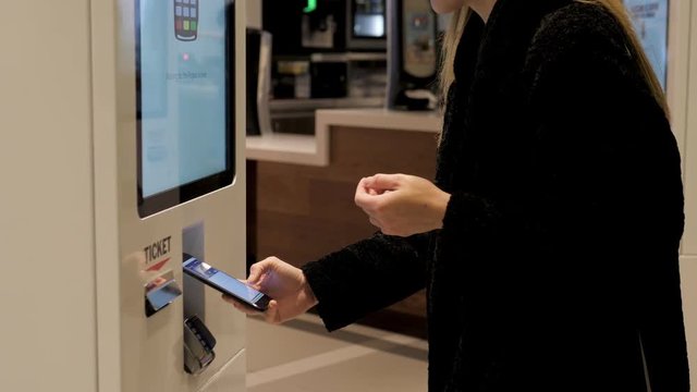 Woman customer store place orders and pay by contactless credit card mobile phone through self pay floor fast food, payment terminal touchscreen big cafe. Paypass.