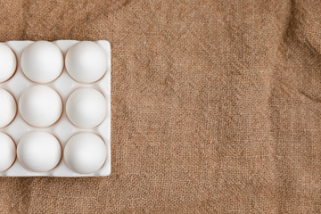 White Chicken Eggs In Ceramic Carton Holder On Burlap Background, Top View, Space For Text