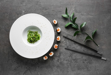 Plate with tasty sushi rolls, algae and chopsticks on grey table