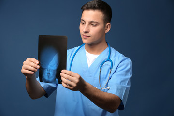 Male doctor studying X-ray image on color background