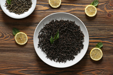 Plates with different types of dry tea leaves and lemon slices on wooden table