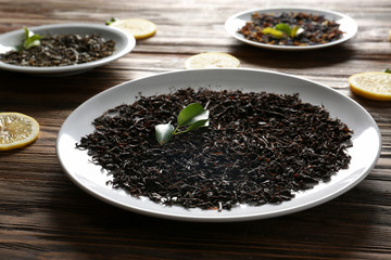 Plates with different types of dry tea leaves and lemon slices on wooden table