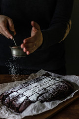 Obraz premium Woman sprinkling powdered sugar on top of brownie
