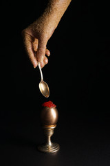 Female hand holding spoon and golden egg with red caviar on dark background