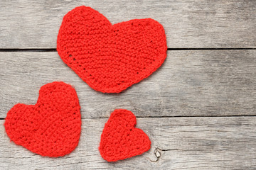 Three red knitted hearts on a gray wooden background, symbolizing love and family