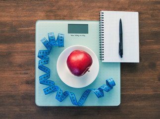The concept of healthy nutrition, fitness and weight loss. Weights, measuring tape, apple, open notebook and pencil on the table.