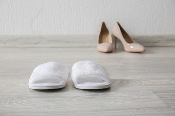 Comfortable slippers and high heeled shoes on floor