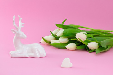 White tulips with deer and heart shaped stone on pink background. Flower flat lay, side view. Floral concept