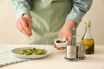 Chef sprinkling tasty ravioli on plate with herbs