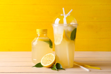 Bottle and plastic cup of fresh lemonade on table - obrazy, fototapety, plakaty
