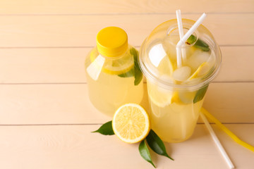 Bottle and plastic cup of fresh lemonade on table