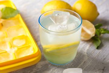 Glass of fresh lemonade and ice tray on table