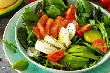 Diet menu concept. Summer Healthy salad with Tomatoes, Salmon, Egg, Avocado and arugula on a dark stone table.