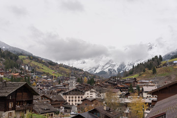 Fototapeta na wymiar Alpine village with high bell tower on the background of the Alps