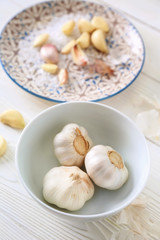 Bowl with fresh garlic on white wooden background