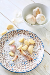 Plate with fresh garlic and salt on white wooden background