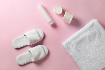 Soft slippers, towel and cosmetics on color background